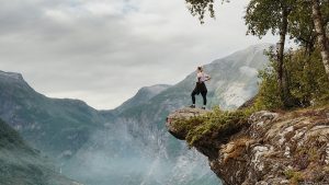 Woman standing on the edge of a cliff with mountains in the background.