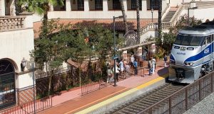 A shot of the Santa Ana Regional Transportation Center. There is an Amtrak train arriving and passengers waiting to load on the platform.