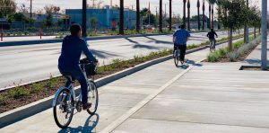 A shot of cyclists using a protected bike lane in Santa Ana, CA. The streets are lined with trees on either side.