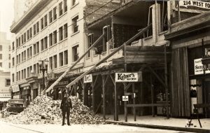 A black and white photo photo of rubble on 4th street and damage to buildings after an earthquake.