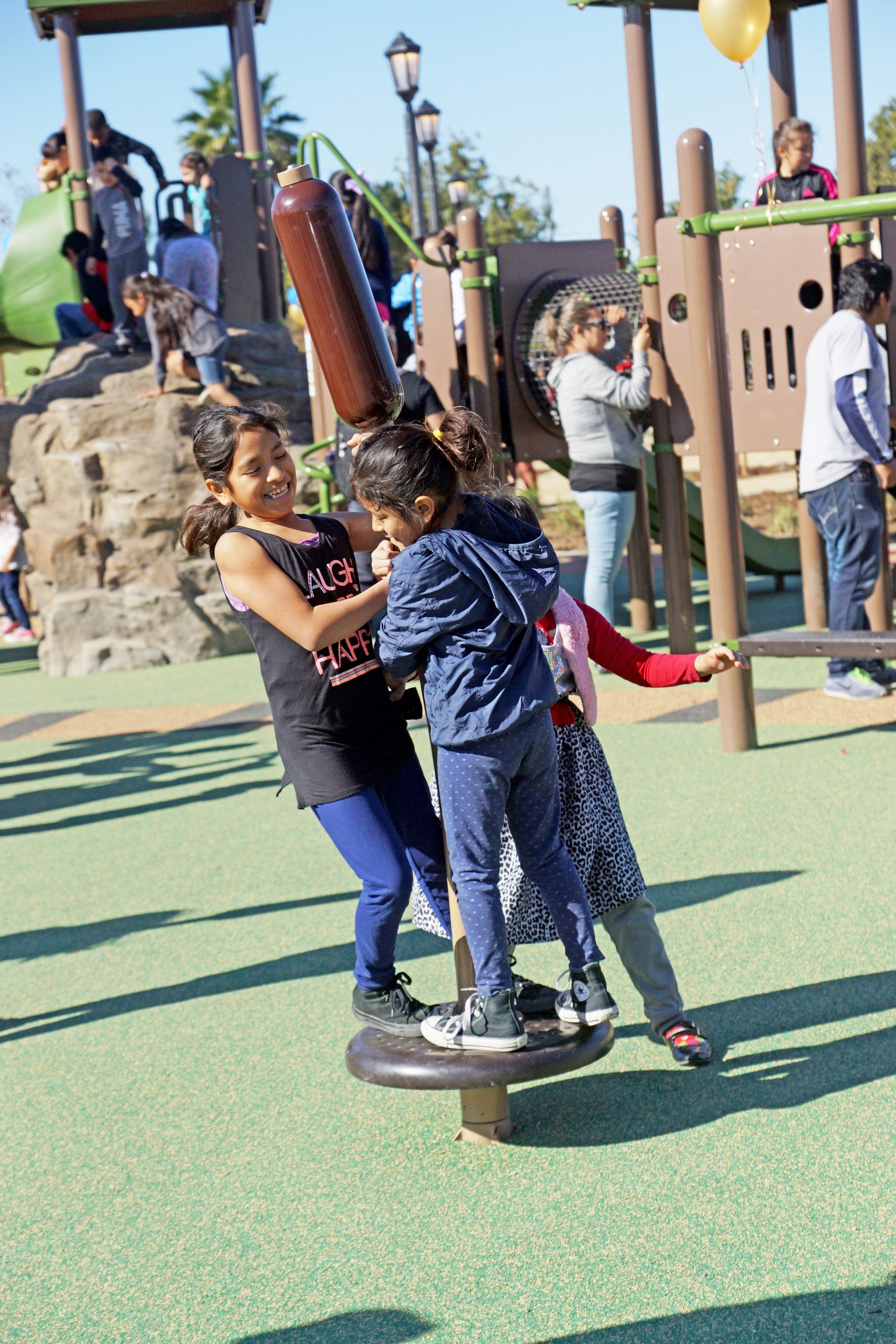 Three young girls playing with a spinning disc at Pacific Electric Park playground in Santa Ana, CA