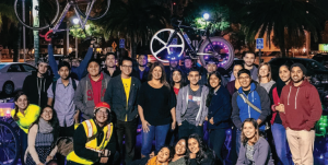 People gather for a group photo. Two people hold up their bikes in the background.