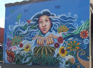 A mural of a woman holding out her hands as flowers grow around her.