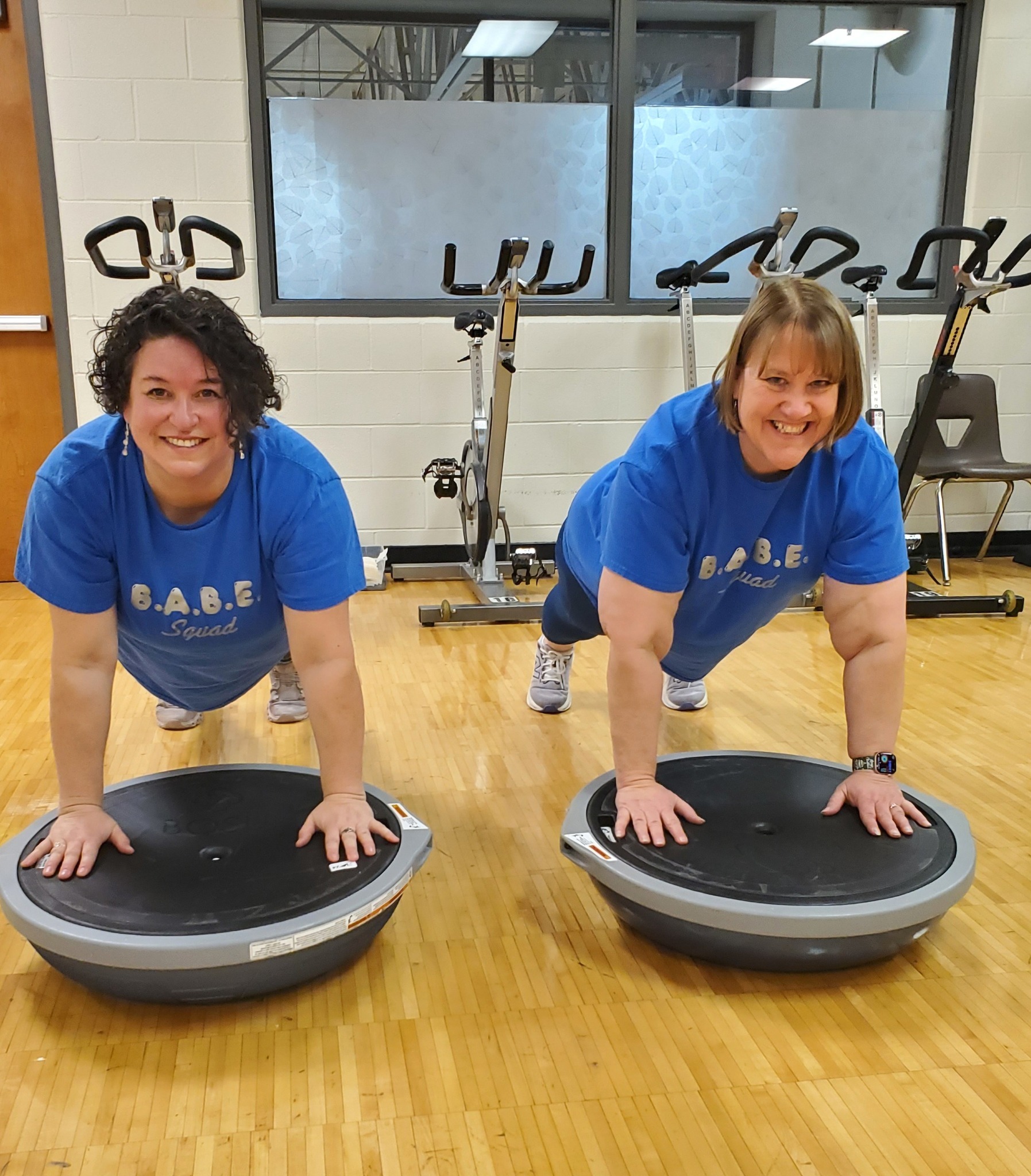 Two ladies in matching blue shirts balancing on exercise balls
