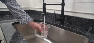 A person filling a cup of water from a faucet