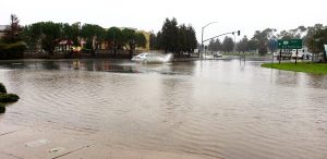 Car driving through a section of flooded roadway.