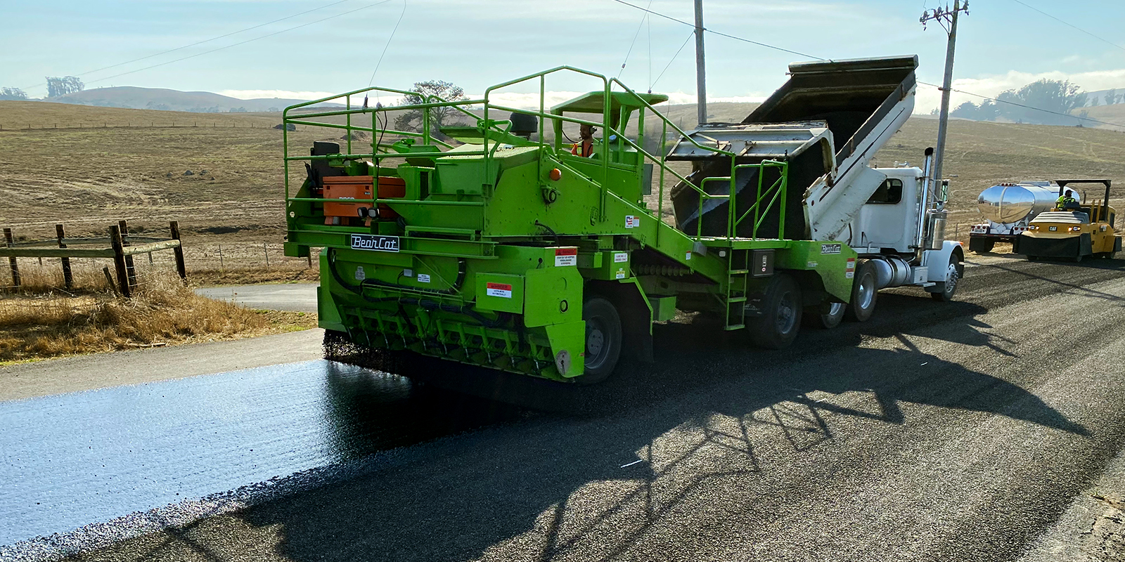 Road work being done on a rural road in West Marin. It is a large green truck laying down new pavement.