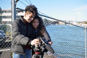 two teenagers stand along San Rafael canal, holding a camera and smiling