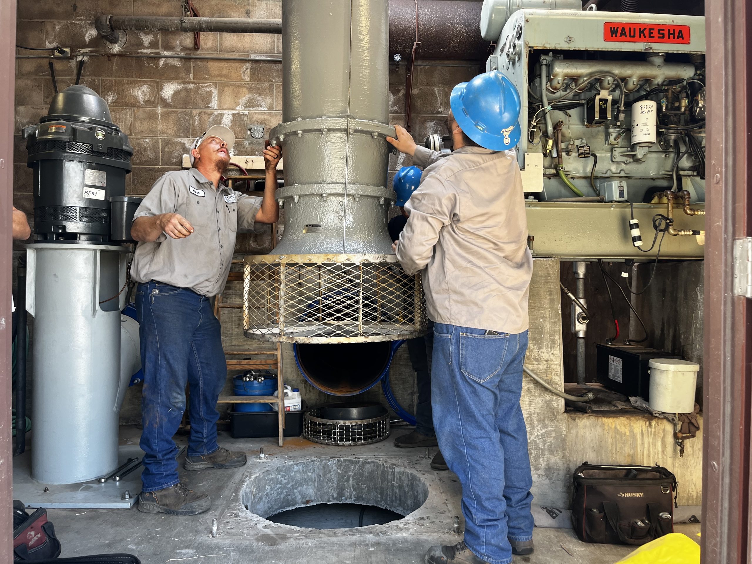 People help guide stormwater pump into place at a County-operated pump station.