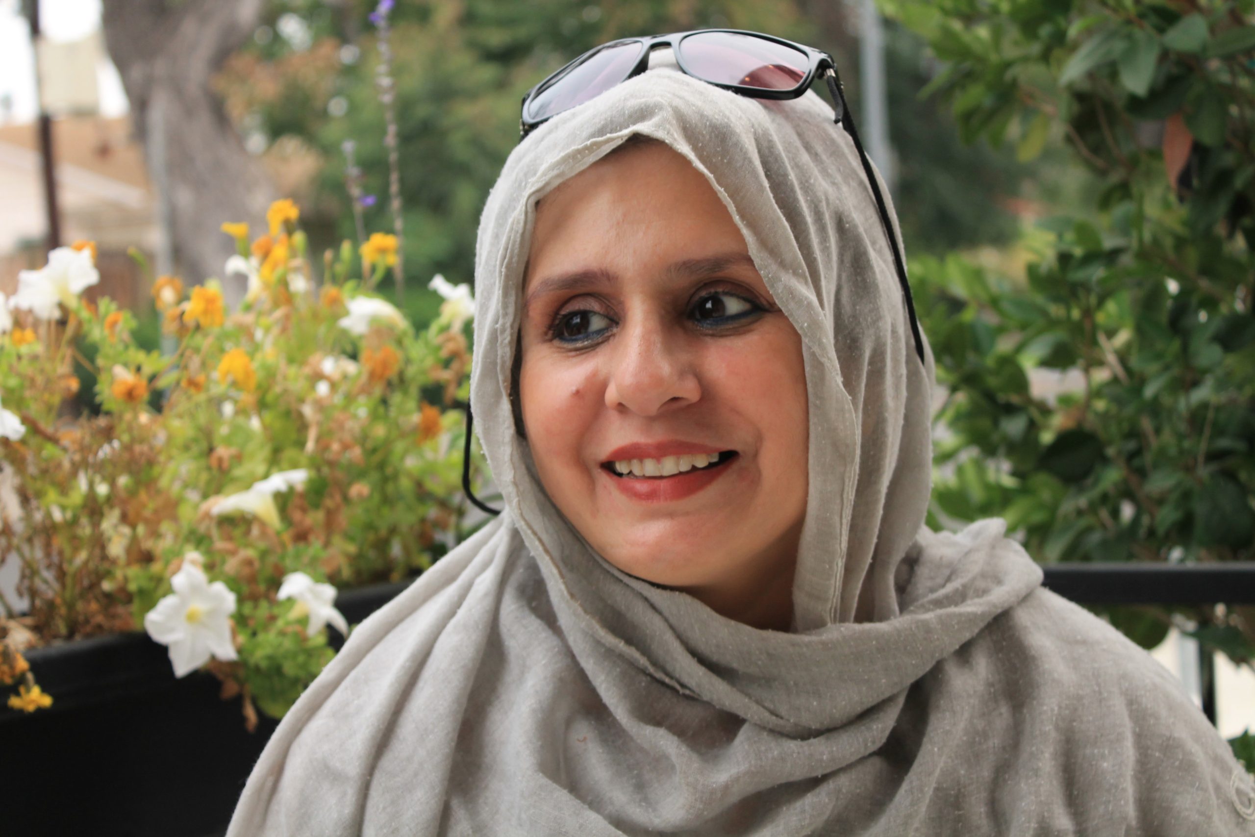 A woman with a grey scarf draped on her head smiles off camera.