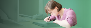 A girl with down syndrome sits at a desk and writes in a notebook