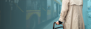 A man in a trenchcoat using a walker waits to board a public bus