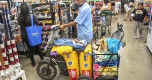 A man with a full shopping cart and a service dog wait to check out at Walmart