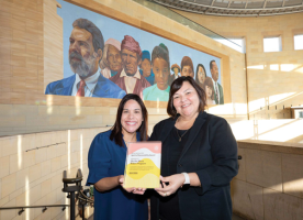 Two women in a Metro station smile while holding an award between them.