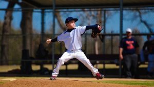 Youth Baseball Pitcher In Wind Up Wearing White Jersey.