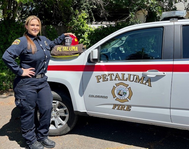 A female fire department employee stands beside a white Petaluma Fire Department vehicle.