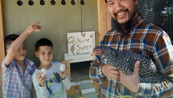 man holding a chicken with two children in the background