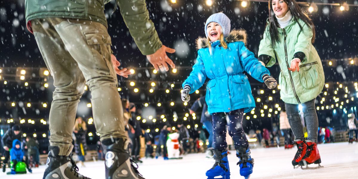 A girl in a blue coat ice skates towards her parent's outstretched arms