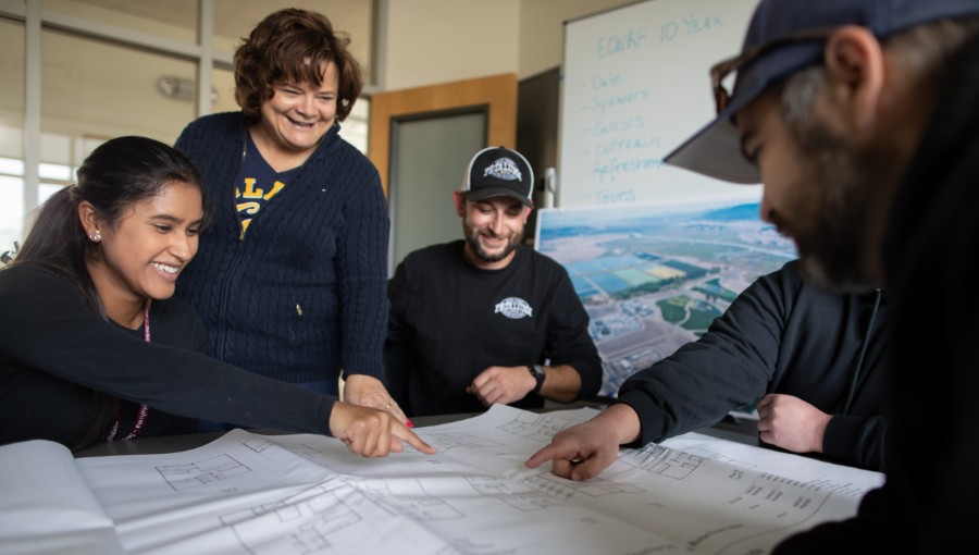 Group of people pointing at a blue print 