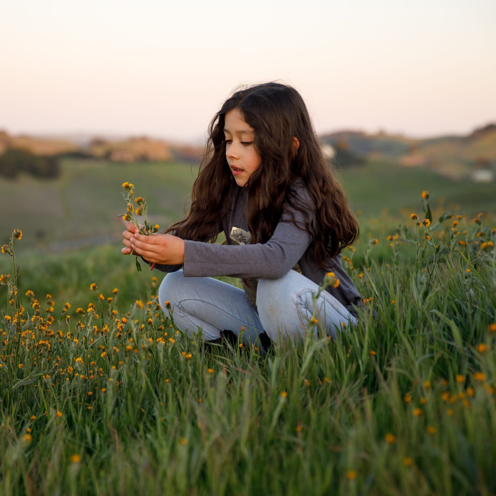 girl sits on a hillside looking at the flowers she holds