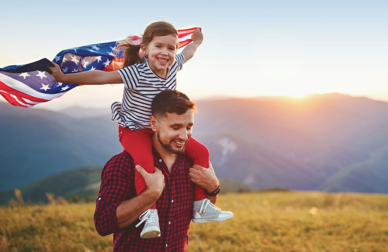 Picture of a parent carrying child on shoulders holding an American flag