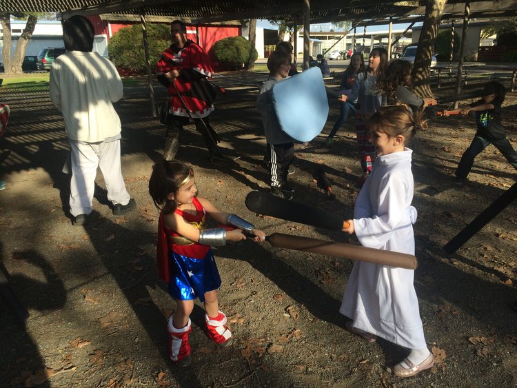 Children dressed as Wonder Woman and Princess Leia play fight near other children in costume.