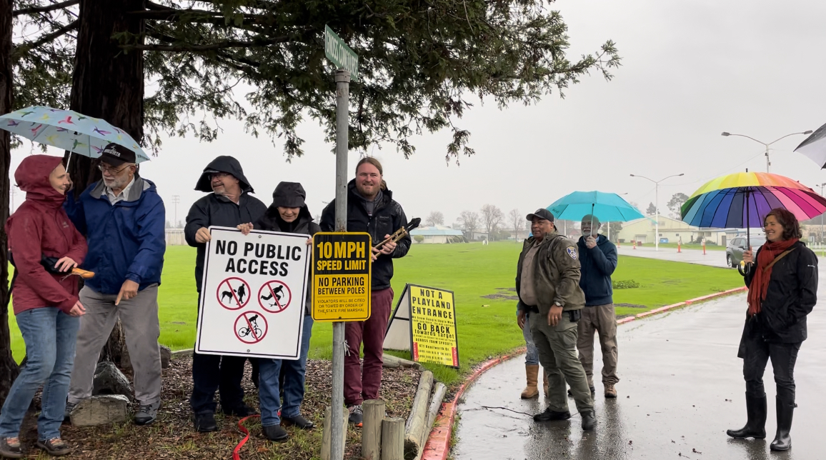 Several community members gather to remove the "No Public Access" sign at the entrance to the Fairgrounds.