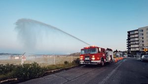 A red fire engine spays water into a blue sky in front of the Puget Sound.
