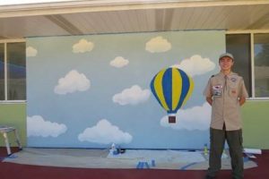 eagle scout posing in front of decorative wall with an air balloon