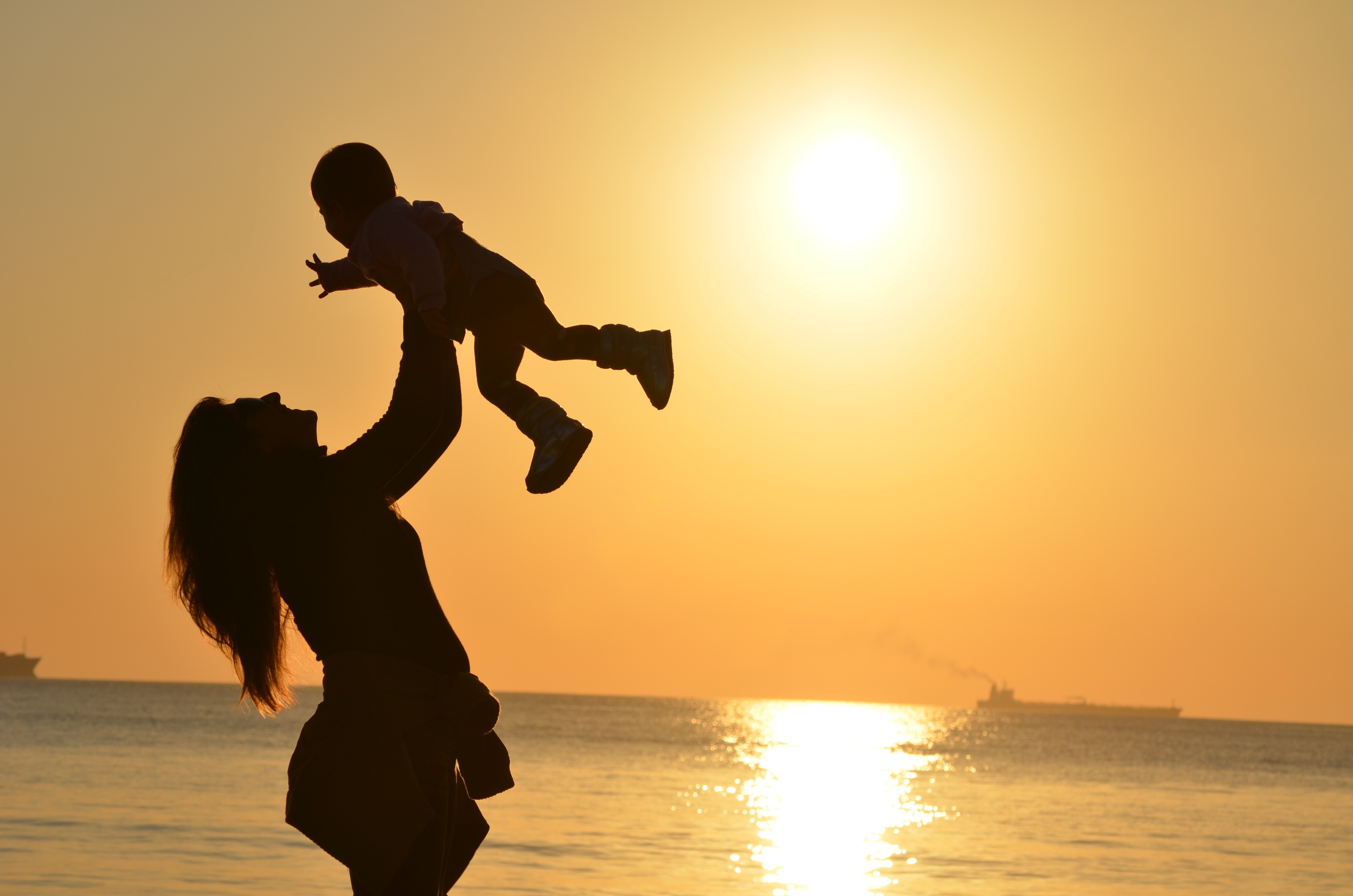 women happily lifting baby up, with the view of a sunset