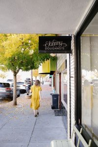 Sidewalk view of San Rafael Street with woman in yellow dress outside Johnny's Donuts.