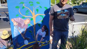 artist near a utility box painted with a newly planted tree