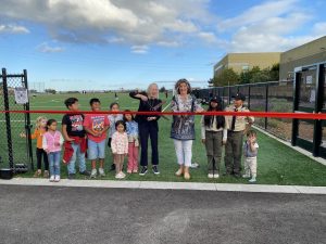 Mayor stands in front of Pickleweed Park soccer field, surrounded by community members, cutting a ribbon.