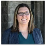 Photo of April Miller in a green shirt, blue blazer and glasses and smiling