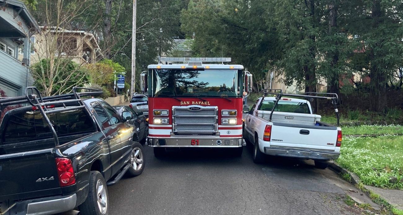 a red engine attempts to squeeze through a roadway with cars parked on both sides