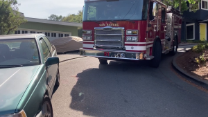 a red fire engine navigates a tight turn and parked car