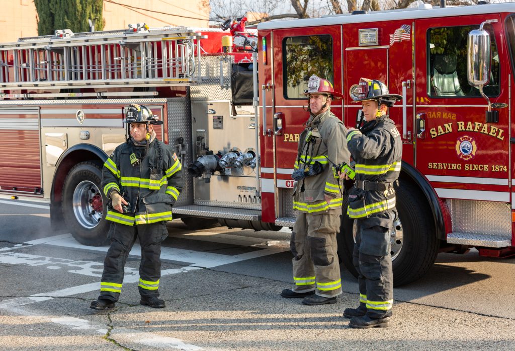 Firefighters stand in front of engine surveying the scene.