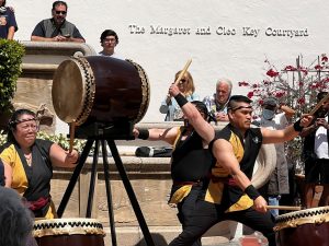 A group of people play large drums.