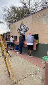 A picture of a group of people working on a wall that has a sign PONY Santa Ana Baseball.