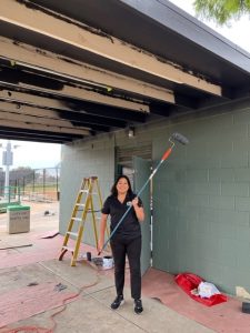 A picture of a person wearing black outfit and painting a wall.