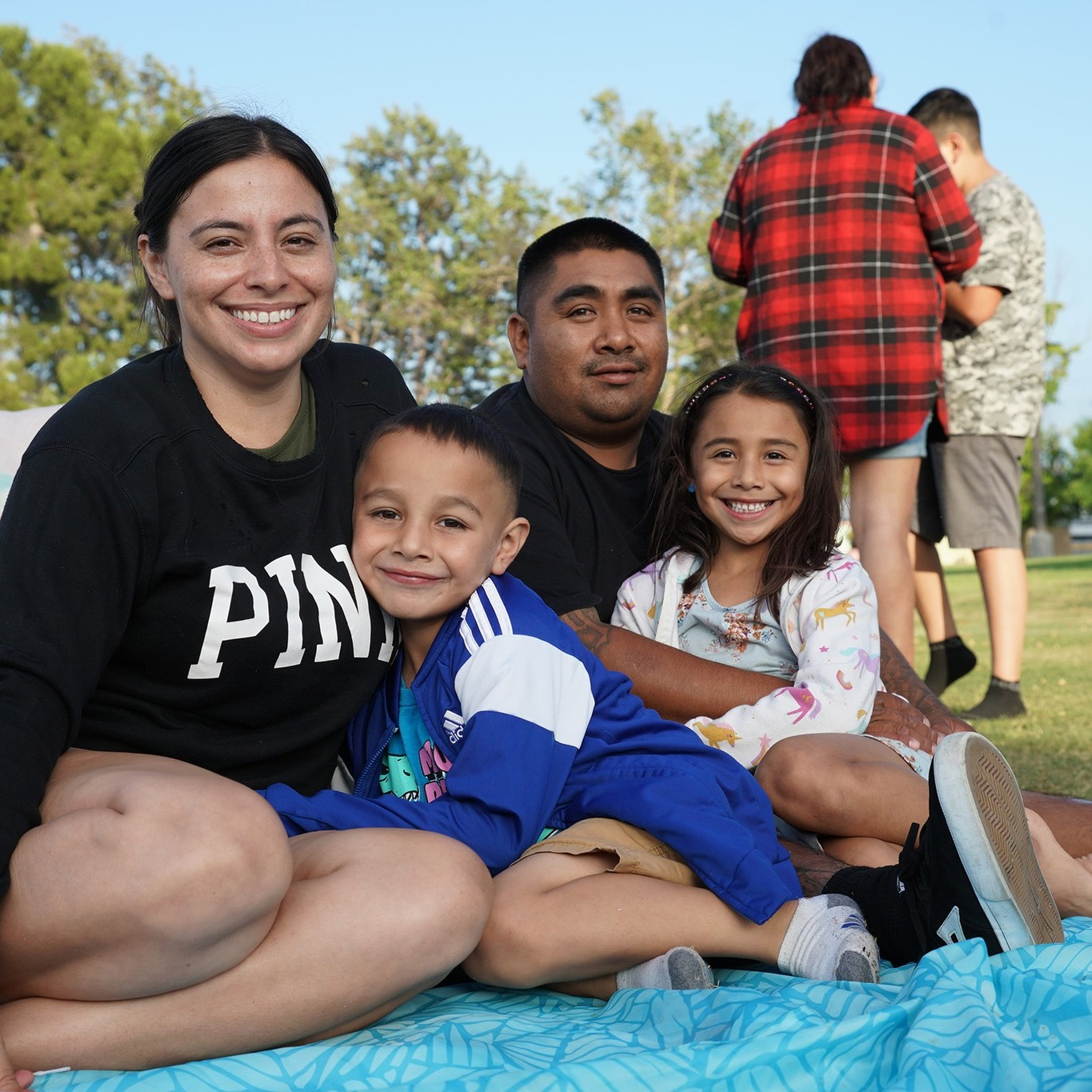 Family sitting on a picnic blanket at a park during a movie showing event