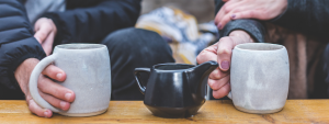 two people holding white mugs next to a black kettle