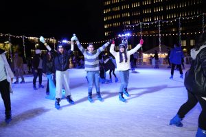 Three skaters pose for a group photo on ice at the Winter Village ice skating rink