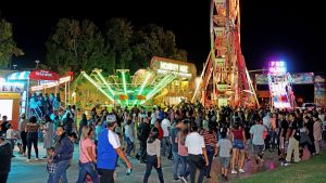 Fiestas Patrias celebration at night with ferris wheel, crowd, and carnival games