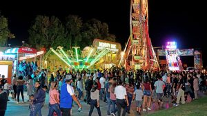 Fiestas Patrias celebration at night with ferris wheel, crowd, and carnival games