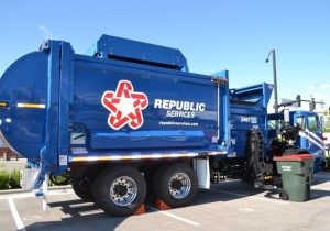 blue Republic Services trash vehicle with Republic Services logo, and green trash bin