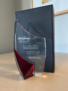 A shaped glass award in front of a black background on a wooden table.
