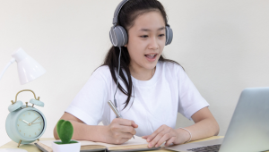 young girl with headphones doing homework on laptop