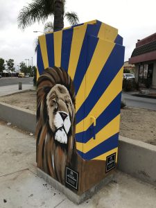 Utility box with art of a lion as the subject and blue and yellow stripes in the background