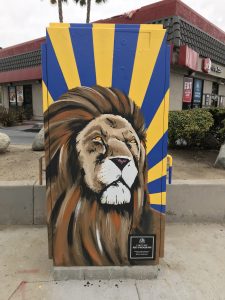 Utility box with art of a lion and blue/yellow stripes in the background